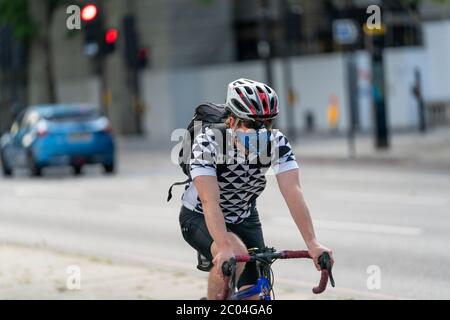 Giovane adulto che cavalca in biciletta in una pista ciclabile per pendolari lungo l'Embankment vicino al Tamigi nel centro di Londra, Inghilterra, indossando un mito facciale Foto Stock
