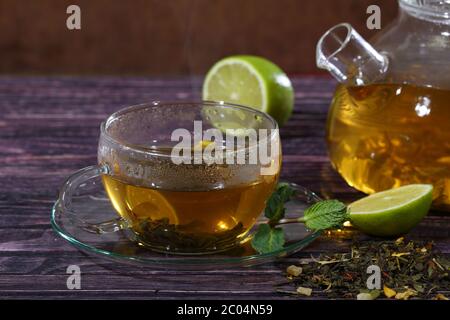 Teiera in vetro e tazza trasparente con tè e aggiunta di menta e lime Foto Stock