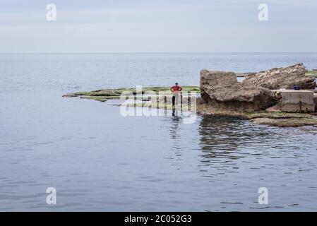 Pescatore vicino alle rovine dell'antico porto di Byblos, la città più grande del Governatorato del Libano del Monte Foto Stock