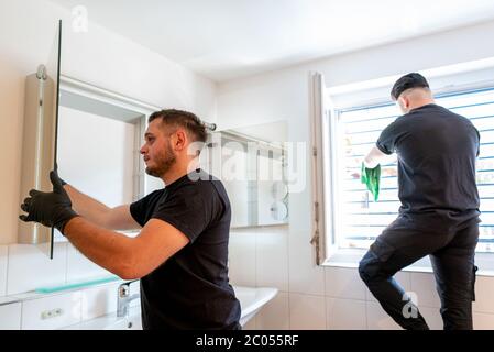 Una vista di due pulitrici professionali in un bagno moderno che pulisce gli armadi e gli specchi e le persiane Foto Stock