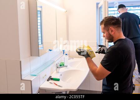 Una vista di due pulitrici professionali in un bagno moderno che pulisce gli armadi e gli specchi e le persiane Foto Stock