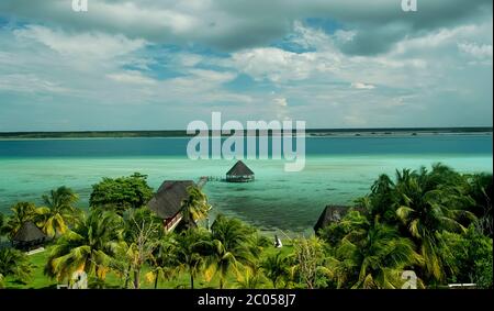 Vista panoramica della laguna di Bacalar, molo in legno e cielo nuvoloso, giardino con palme e gazebo. Il luogo ideale per rilassarsi e meditare Foto Stock