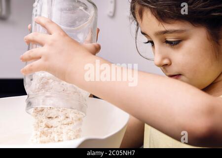bambina che versa la farina in una ciotola per preparare il pane fatto in casa, concetto di cibo sano a casa Foto Stock