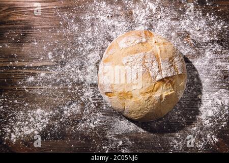 pane rustico appena sfornato su un tavolo di legno pieno di farina, concetto di cibo sano a casa, spazio di copia per il testo Foto Stock