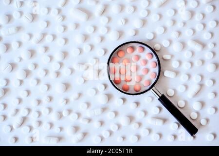 Concetto di assistenza sanitaria, medicina, farmacia, COVID-19, coronavirus. Assortimento di prodotti farmaceutici, pillole bianche e rosa con lente d'ingrandimento Foto Stock