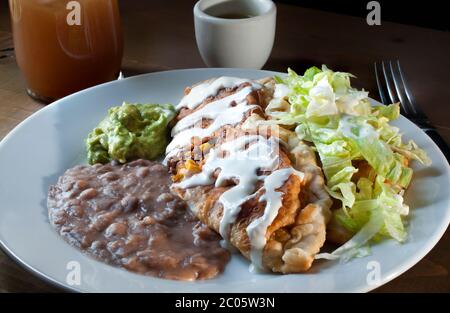 Cibo messicano, empanadas di manzo con un lato di guacamole, fagioli e lattuga con panna sulla parte superiore e una tazza bianca di salsa piccante e una bevanda di tamarindo. Foto Stock