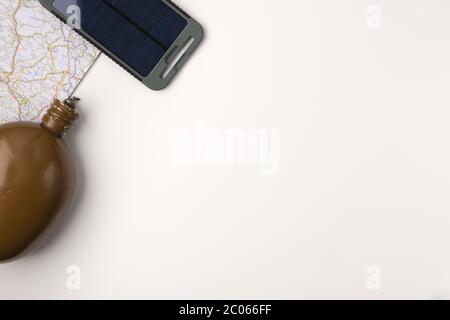 Accessori per viaggiatori. Mappa con bottiglia d'acqua vintage e pannello solare portatile su sfondo bianco con spazio vuoto per il testo. Concetto di vacanza di viaggio. S Foto Stock