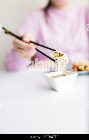 Le donne divulghano il gustoso sushi roll con le trichette nel recipiente con salsa di soia al tavolo. Foto Stock
