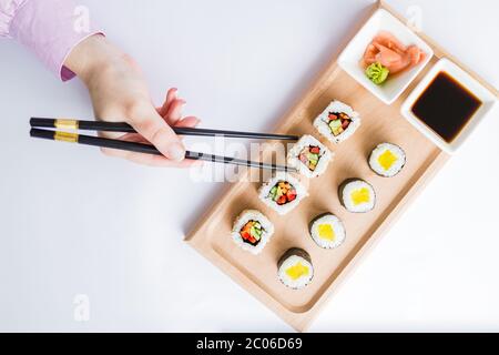 Posa piatta della mano femminile con le bacchette per mangiare set di panini sushi. Foto Stock