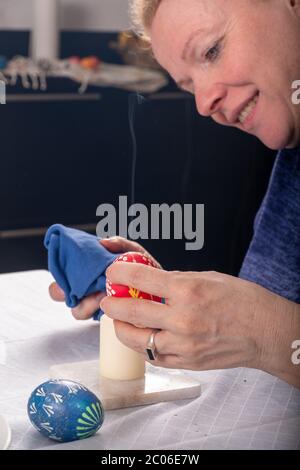 sorbian rosso testa le mani delle donne rimuovono con una candela fiamma la cera secondo la tradizione sorbiana dell'uovo di Pasqua rosso multicolore Foto Stock