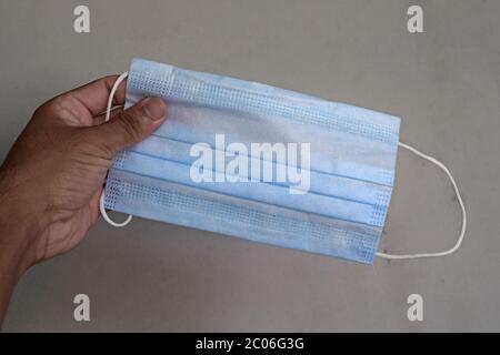 Mano che tiene una maschera chirurgica per la protezione da virus Foto Stock
