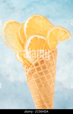 Fette di agrumi essiccate in un cono gelato a base di waffle su sfondo blu con spazio per la copia Foto Stock