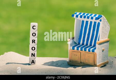 Simbolo per le vacanze durante la crisi della corona. I dadi formano la parola 'corona' accanto ad una sedia da spiaggia. Foto Stock