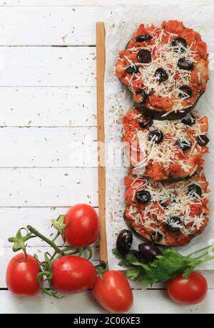 Concetto di cibo fatto in casa. Melanzane al forno gratinate con pomodori, olive e parmigiano su tavola di legno bianco. Vista dall'alto. Foto Stock