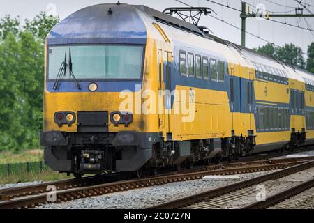 Un tipico treno olandese giallo-blu, un po' sporco, corre sulle rotaie vicino alla stazione di Heerenveen, Paesi Bassi. Mettere a fuoco sulla parte anteriore della locomotiva Foto Stock