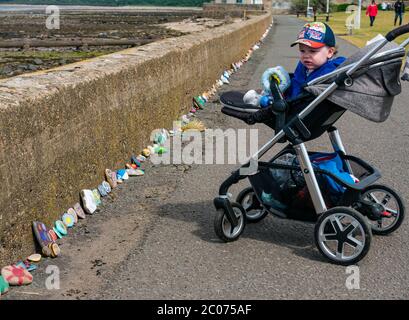 Port Seton, East Lothian, Scozia, Regno Unito. 11 Giugno 2020. Covid-19 simboli pandemici creati dalla gente del posto: Una linea lunga centinaia di piedi sul lungomare di pietre colorate e creative dipinte a mano con messaggi ispiranti. Sembra essere un fenomeno che si diffonde intorno alle città e villaggi della Lotia orientale. Max, di età compresa tra 18 e 30 mesi, è interessato a guardare le pietre colorate Foto Stock