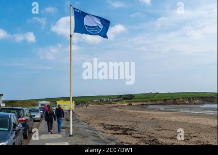 Garretstown, West Cork, Irlanda. 11 Giugno 2020. Nonostante i venti di forza di Gale, sia i locali che i turisti sono andati alla spiaggia di Garrettstown oggi. Una coppia cammina oltre la bandiera Blue Beach 2020 che Garretstown Beach ha raggiunto quest'anno, una delle otto spiagge della contea di Cork per ottenere il premio. Credit: Notizie dal vivo di AG/Alamy Foto Stock