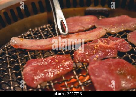 Pinzette che girano il migliore manzo giapponese succoso su una griglia con fiamme di carbone Foto Stock