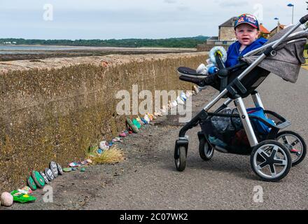 Port Seton, East Lothian, Scozia, Regno Unito. 11 Giugno 2020. Covid-19 simboli pandemici creati dalla gente del posto: Una linea lunga centinaia di piedi sul lungomare di pietre colorate e creative dipinte a mano con messaggi ispiranti. Sembra essere un fenomeno che si diffonde intorno alle città e villaggi della Lotia orientale. Max, di età compresa tra 18 e 30 mesi, è interessato a guardare le pietre colorate Foto Stock