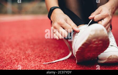 chiudi la foto di una ragazza caucasica che prepara le scarpe per una sessione di jogging in uno stadio sportivo rosso Foto Stock