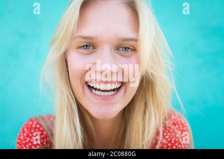 Una bella donna bionda sorridente durante una giornata di sole davanti a uno sfondo turchese Foto Stock