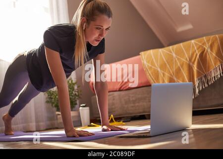 Giovane donna che partecipa a una lezione di fitness online di fronte al computer portatile. Foto Stock