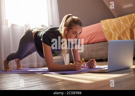 Giovane donna che partecipa a una lezione di fitness online di fronte al computer portatile. Foto Stock