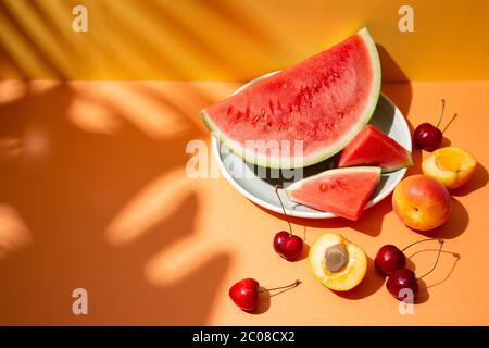 Composizione di frutta estiva alla moda con foglie tropicali ombreggiate su un set arancione e giallo. Spazio di copia Foto Stock