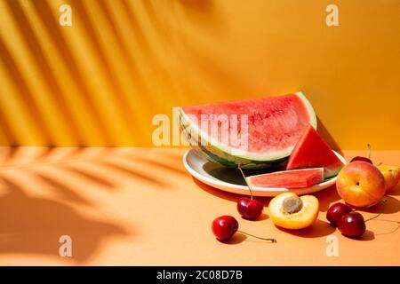 Composizione di frutta estiva alla moda con foglie tropicali ombreggiate su un set arancione e giallo. Spazio di copia Foto Stock