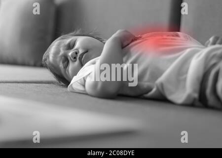 Un piccolo bambino che si stendeva sul letto malato, piangendo per il suo stomaco che fa male. Bianco e nero, rosso isolato. Foto Stock