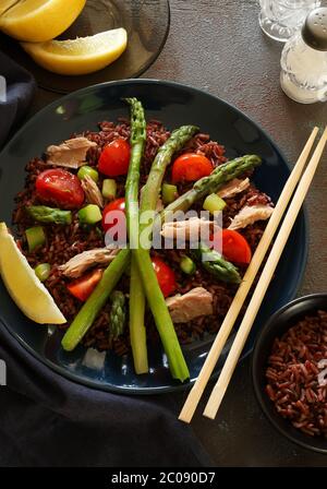 Concetto di cibo sano. Insalata fresca con riso rosso, tonno, asparagi, pomodori e limone su fondo scuro. Vista dall'alto. Foto Stock