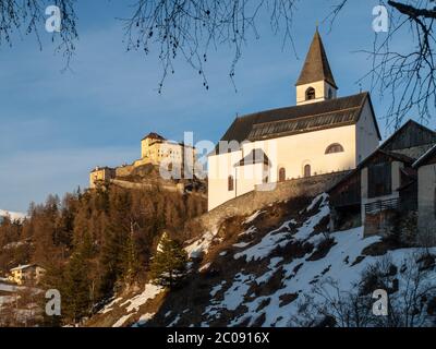 Piccola chiesa rurale e castello sullo sfondo nel villaggio di Tarasp, Graubunden, Svizzera Foto Stock