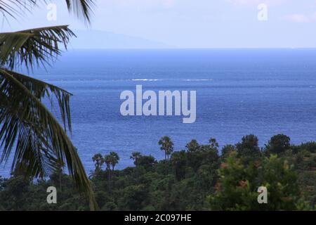 Isola di Lombok vista da Bali Est, sul mare con palme su un lato e un'onda che si forma in lontananza Foto Stock