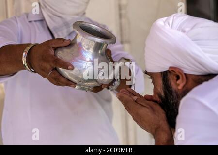 Un volontario sikh che offre acqua Santa all'interno di Bangla Sahib Gurudwara, dopo l'apertura della maggior parte dei luoghi religiosi come l'India facilita la limitazione di blocco Foto Stock