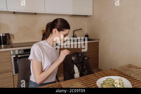 felice giovane donna che tiene affettato avocado e guardando il bulldog francese Foto Stock