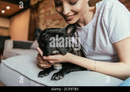 giovane donna sorridente e toccante bulldog francese nero a casa Foto Stock