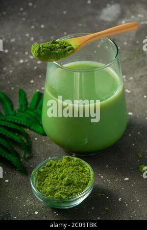 Fuoco selettivo, tè giapponese matcha verde con latte, con un cucchiaio di legno e fogliame su sfondo scuro Foto Stock