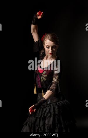 giovane ballerina di flamenco in abito che tiene castanets mentre balla isolato su nero Foto Stock