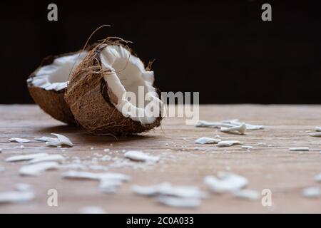 fuoco selettivo di fresche e gustose metà di cocco e fiocchi su tavola di legno isolato su nero Foto Stock