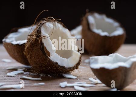 fuoco selettivo di fresche e gustose metà di cocco e fiocchi su tavola di legno isolato su nero Foto Stock