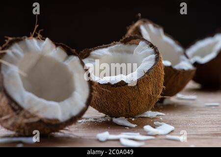 fuoco selettivo di fresche e gustose metà di cocco e fiocchi su tavola di legno isolato su nero Foto Stock