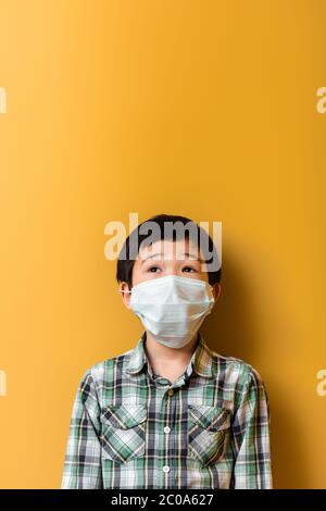 sorprende ragazzo asiatico in maschera medica sul giallo durante l'auto isolamento Foto Stock