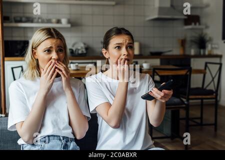 Sorelle scioccate e spavate che guardano la tv sul divano a casa Foto Stock