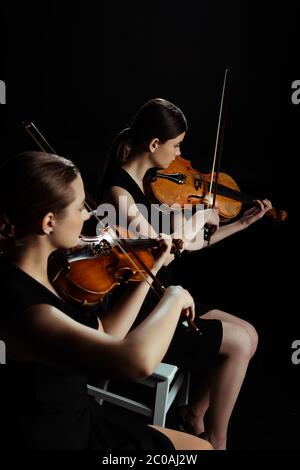 due musicisti professionisti che suonano musica classica sui violini su un palcoscenico scuro Foto Stock