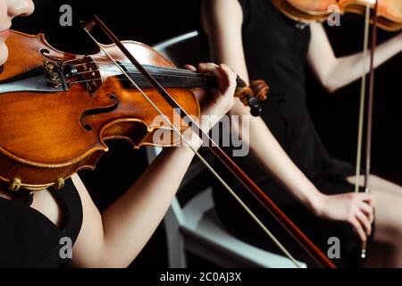 vista ritagliata di due musicisti professionisti che suonano su violini su un palcoscenico scuro Foto Stock