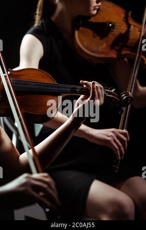 vista parziale di due musicisti professionisti che suonano su violini su un palcoscenico scuro Foto Stock