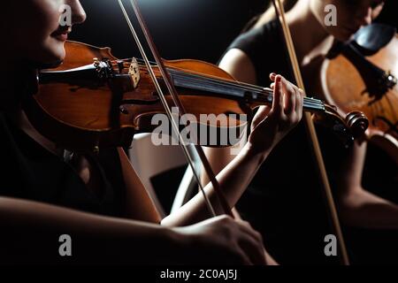 vista ritagliata di due musicisti professionisti che suonano su violini su un palcoscenico scuro Foto Stock