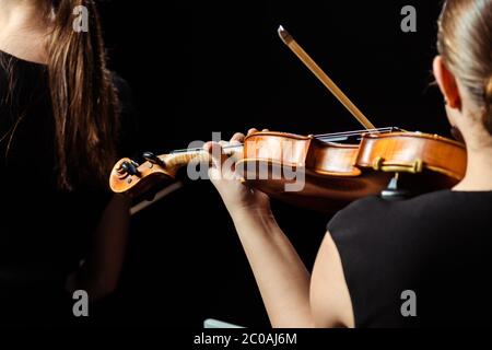 indietro vista ritagliata di due musicisti professionisti che suonano su violini su un palcoscenico scuro Foto Stock