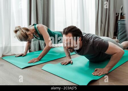 Vista ad angolo basso di un uomo sorridente che si allea sul tappetino fitness vicino alla moglie a casa Foto Stock