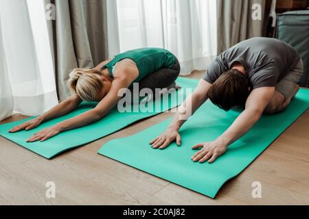 Vista ad angolo basso di coppie mature che si allungano su materassini fitness a casa Foto Stock